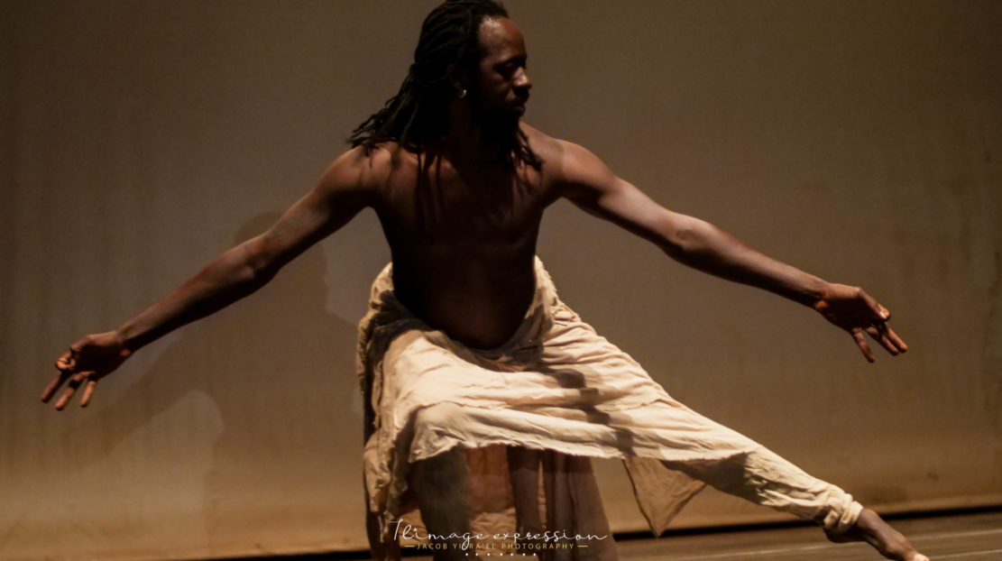 Aguibou Bougobali Sanou dancing on a stage with arms reaching to either side