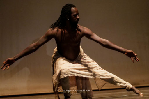 Aguibou Bougobali Sanou dancing on a stage with arms reaching to either side