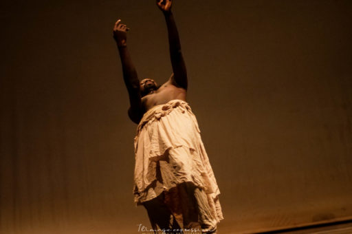 Aguibou Bougobali Sanou dancing in a stage with arms raised.