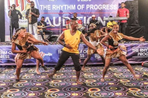 Nicholas Akas dances with a group. They are in a space with decorative walls and flooring. Akas is standing in the front. There are 4 people behind him. They are wearing a mix of attire with yellow and black colors.