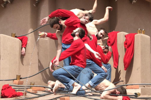 Photo of a dance work by David Harvey featuring a group of male dancers in a formation wearing red shirts and blue jeans.