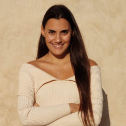 Constantina Theofanopoulou 1 - Constantina Theofanopoulou headshot. She is wearing a cream sweater against a beige background. She has long brown hair and is crossing her arms while looking at the camera smiling.