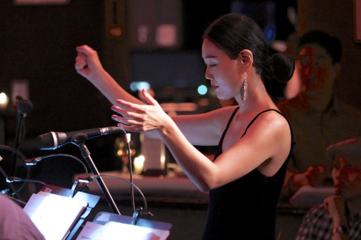 Jihye Lee conducts a jazz band. She is on the right with her arms up and the jazz band is on the left. The saxophone section is in the front.