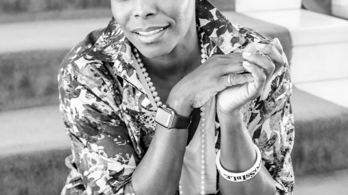 Hope Boykin headshot in black and white. Hope Boykin is sitting down with her hands in a clasped position near her face. She is wearing a patterned dress and a long, pearl necklace. Hope has short, dark hair and she identifies as a Black woman.