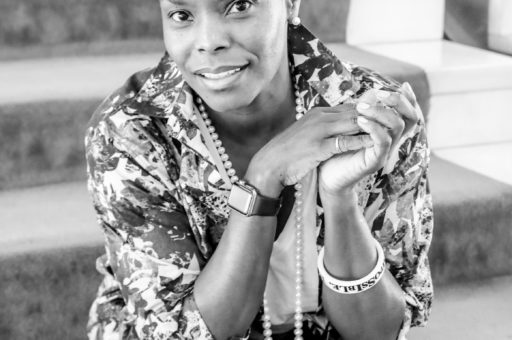 Hope Boykin headshot in black and white. Hope Boykin is sitting down with her hands in a clasped position near her face. She is wearing a patterned dress and a long, pearl necklace. Hope has short, dark hair and she identifies as a Black woman.