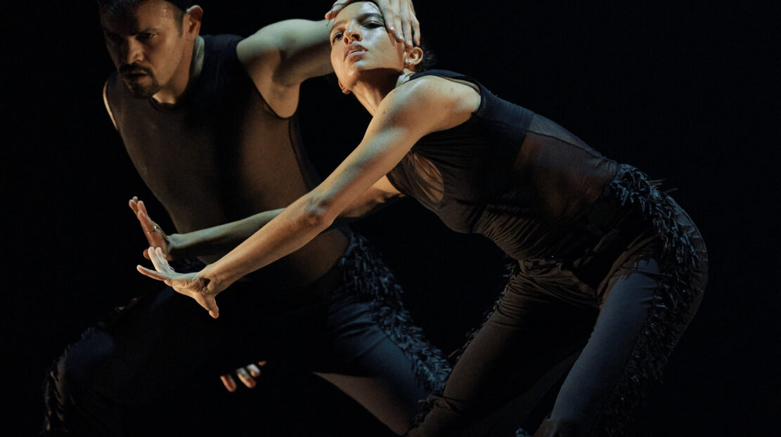 Ausia Jones dancing with other dancers and wearing black against a black background.