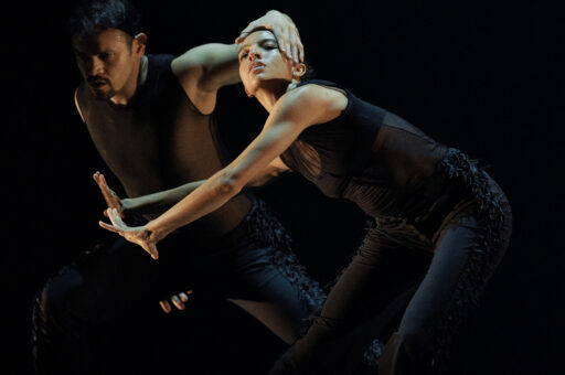 Ausia Jones dancing with other dancers and wearing black against a black background.