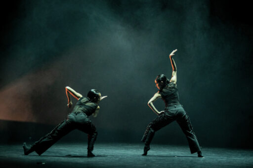 Ausia Jones, dancing with another dancer wearing black against a black background, surrounded by smoke.