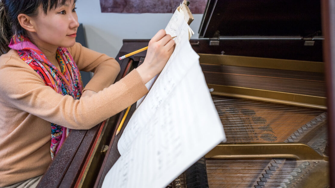 Photo of Wang Lu at a piano writing music.