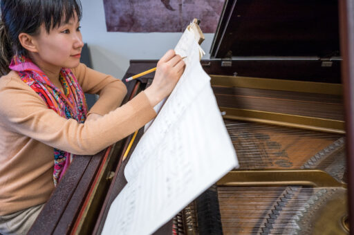 Photo of Wang Lu at a piano writing music.