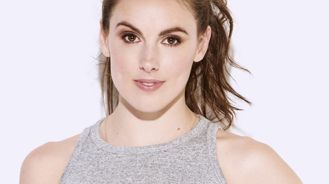 Headshot of Tiler Peck, who has brunette, long, wavy hair in a ponytail, fair skin, and standing against a white background.